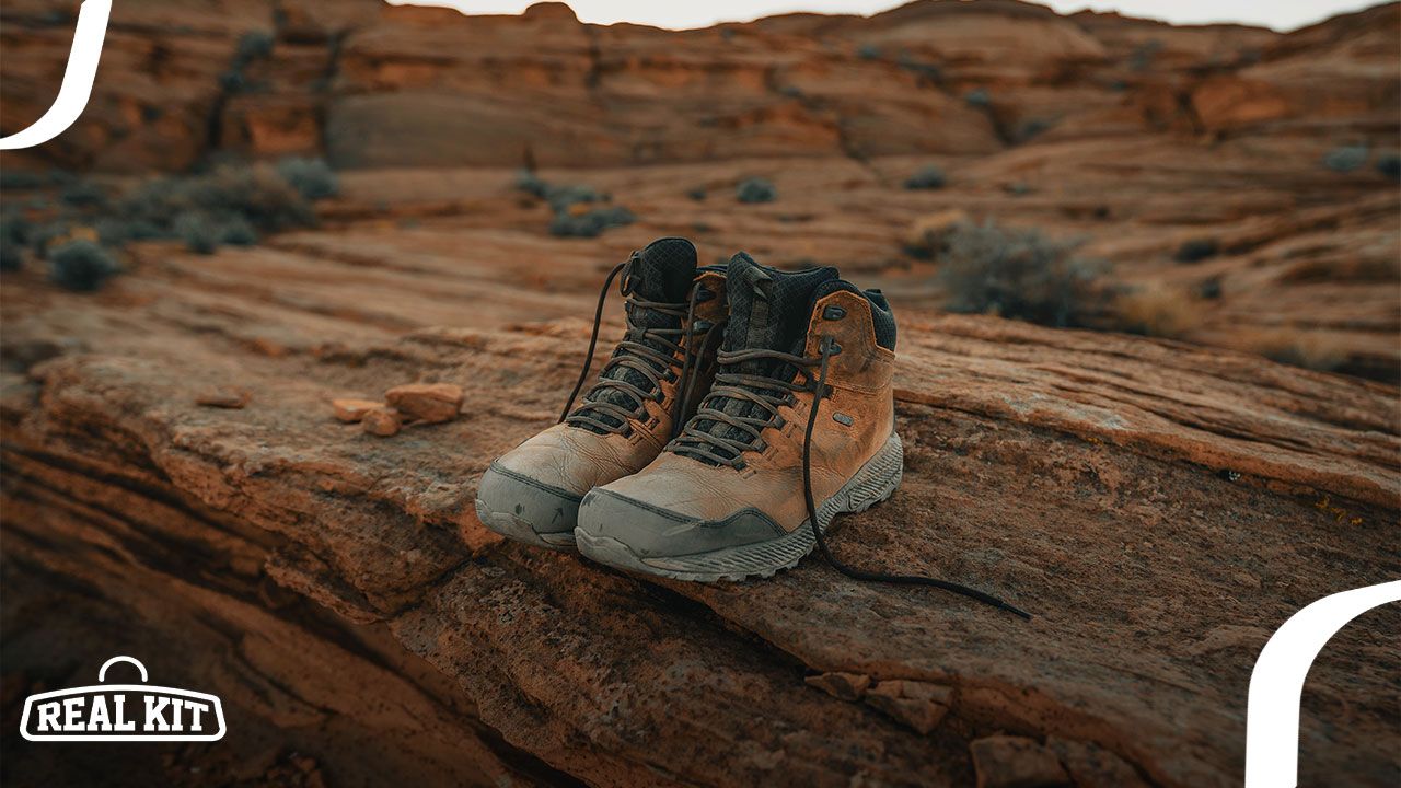 A pair of light brown hiking boots with black laces and tongues sat on the edge of an orange-rock cliff.