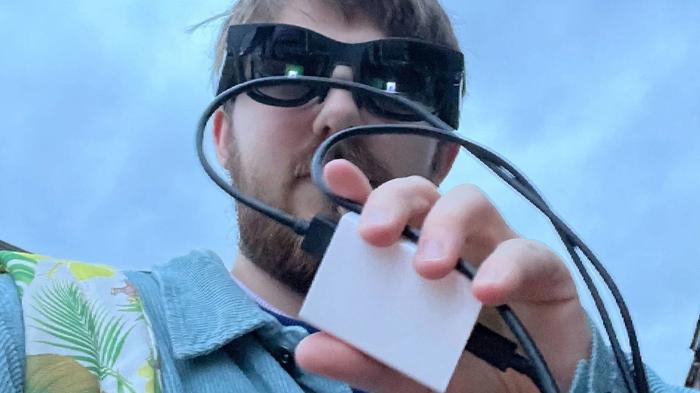 White man using NReal Air AR glasses and adapter outside. 